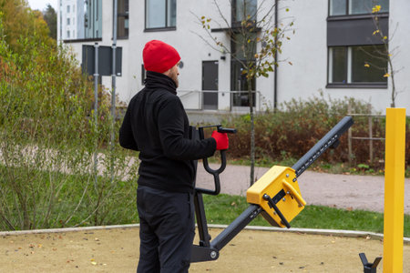 A man is exercising on an outdoor Chest Press Machine in a public place in Finland on an autumn day. An active urban lifestyle, self-discipline, healthy habits, and the importance of staying physically active throughout the year