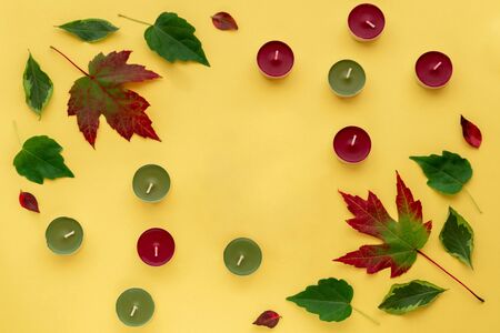 Autumn leaves flat lay. Frame from red green leaves and candles on yellow paper background. Autumn composition top view. Copy spaceの写真素材