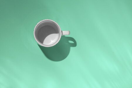 Empty tea cup on mint paper background. Coffee mug from above. Minimal concept. Long shadow with reflections. Flat lay, top view.の写真素材