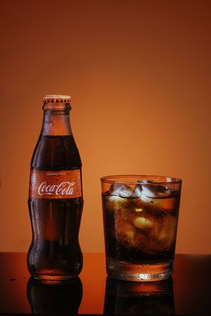 Italy, Milan - 15 November 2019: Classic bottle Of Coca-Cola and glass of fresh Coca Cola with ice...