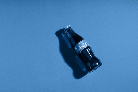 Coca Cola in glass bottle on blue paper background. Trendy color of the year 2020. Italy, Milan - 15 November 2019のeditorial素材