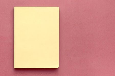 Top view of closed yellow cover notebook on pink desk background. Business concept. Top view, flat...