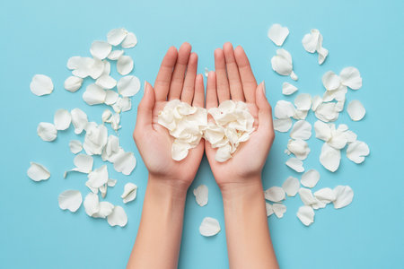 Gentle hands holding white petals on blue background for spa and wellness concept design.の素材