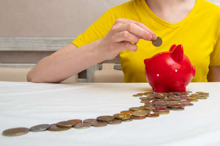 Line of moent that lead to female hands put a coin in the slot of the red piggy bank.の写真素材