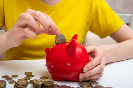 woman hand put money coins in a red piggy bank to save money, a few coins on the table. The concept of financial economy, crisisの写真素材