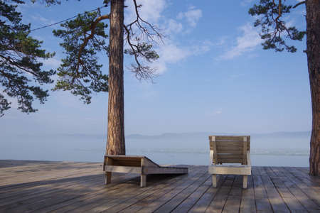 Spring morning, by the lake on which the snow melts, there are two empty deck chairs, pine trees grow nearby, there are no people around. The concept of loneliness, relaxationの写真素材