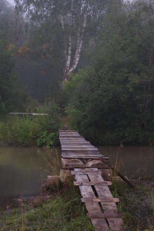 Front view of the landscape with a small old wooden suspension bridge for people traveling across the river.の写真素材