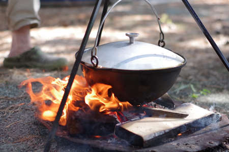 A large metal pot with a lid and a handle on a tripod for cooking on a camping trip, outdoor activities.の写真素材