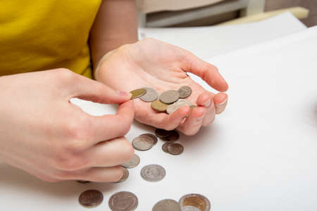 Saving money, a hand puts coins in another hand, on a light table are coins of different countries, close-up.の写真素材
