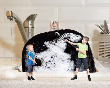 creative work: three miniature children wash a large black plate with foam. Homework concept.の写真素材