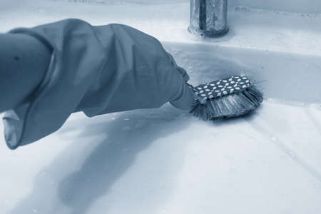 A hand in a yellow glove cleans the bathroom with a blue brush on the handle. The concept of homework, disinfection. Classic blue, trend 2020の写真素材