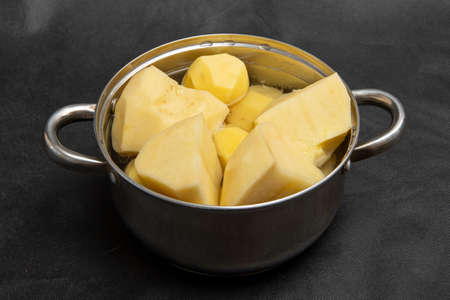 Home kitchen. Casserole, a bowl of peeled and chopped potatoes on a black background, close-up, top view.の写真素材