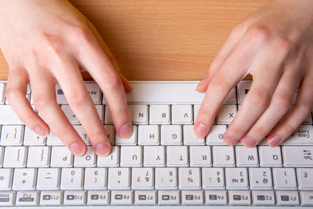 two female hand is typing on a white keyboard with English letters, close-up, selective focus. The concept of home schooling, distance learningの写真素材