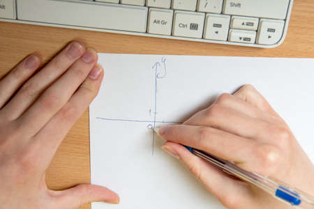 Female hand draws an axis for plotting, math homework, close-up. Home teaching concept.の写真素材