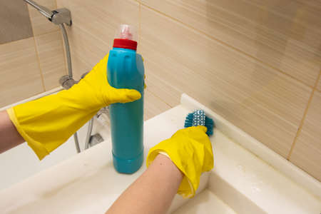Hands in yellow gloves cleans the white bath with a cleaning agent and a blue sponge on the handle. The concept of homework, disinfectionの写真素材