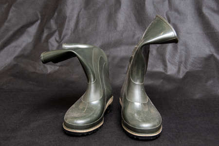 Rumpled dark rubber boots stand on a dark background.の写真素材