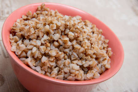 Closeup buckwheat porridge in a tipped pink clay bowl. Side view, selective focus. Healthy eating concept.の写真素材