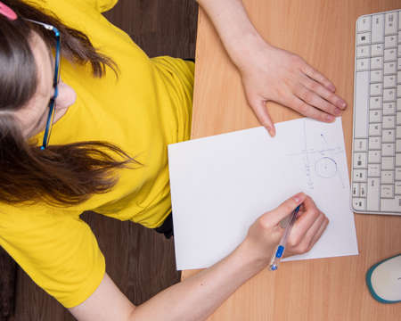 Portrait of a beautiful serious Caucasian girl in a yellow T-shirt, writes a schedule, work at home, distance learning.の写真素材