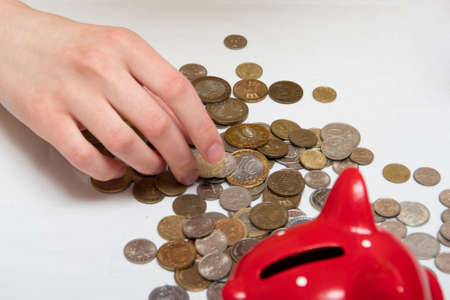 many coins of different countries lie on the table near the red piggy bank. Financial concept.の写真素材