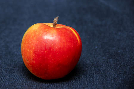 One ripe fresh organic sweet red apple with yellow spots, close-up, on a blue jeans background.の写真素材