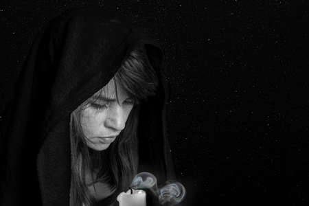 Close-up of a woman's face in a black shawl and an extinct candle. Black and white. The concept of...