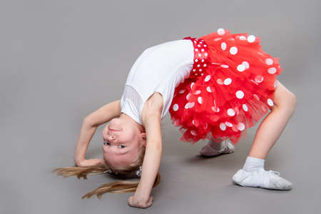 A little girl in a white T-shirt and red skirt does an exercise bridge. The idea of sports, fitness at home. Self-isolation.の写真素材