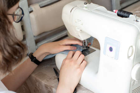 Close-up of sewing on a sewing machine, selective focus. The girl in glasses sews clothes. The...
