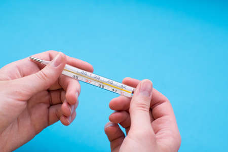 Close-up female hand holds a thermometer on a blue background. Thermometer shows a high body temperature.の写真素材
