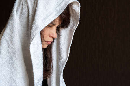 Close-up of a womans face in a white scarf on a dark blue background, embarrassment, sadness, sadnessの写真素材