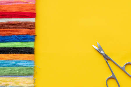 Multi-colored thread for embroidery laid out in a row and scissors on a yellow background. Top view, copy space, flatlyの写真素材