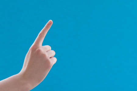 Caucasian white female hand with forefinger raised up and pointing, on blue background, copy space.の写真素材