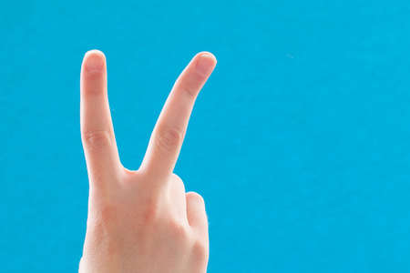Close-up hand with two fingers up in a symbol of peace or victory. Also a sign for the letter V in...