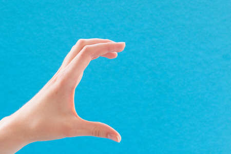 Female caucasian hand on a blue background showing gesture of taking something, grabbing, closeupの写真素材