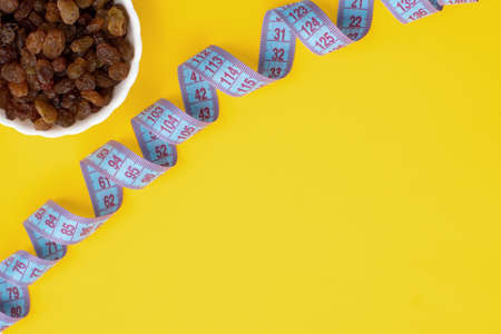 Close-up plate with dried fruits raisins and a centimeter tape. The concept of weight loss, healthy...