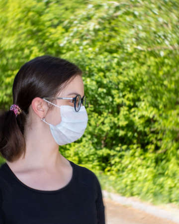 Close-up portrait of a beautiful young woman wearing a disposable medical face mask in a public place because of the Covid-19 epidemicの写真素材