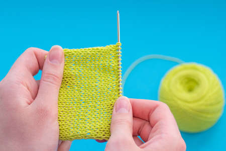 Close up of hands of caucasian woman knitting with green thread on a blue background, ready pattern,...
