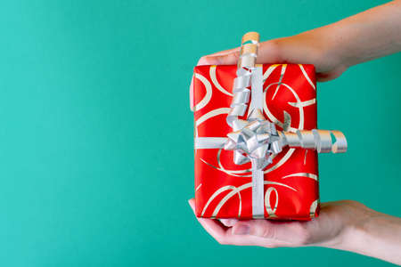 Top view of female hands holding a gift in red packaging on a green background. Creativity concept, handmade, holiday, new year and christmas.の写真素材
