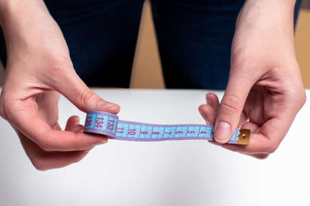 Female hands hold blue tape measure, tape measure for measuring size on a light background.の写真素材