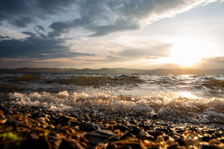 Sunset on a stormy lake with splashes from large waves. Big waves with foam and spray. Beautiful...