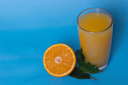 Fresh orange juice in a glass with fruit cut in half and sliced by green leaves isolated on a blue background, top view, copy spaceの写真素材