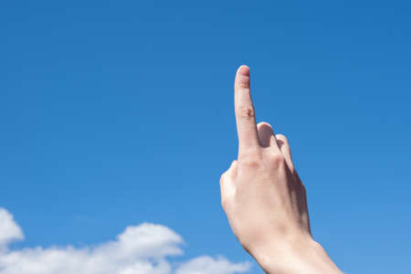 Close-up female hand with index finger up on a background of blue sky with clouds, copy space.