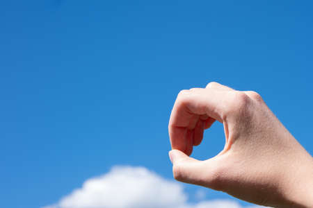 Close-up gesture of a woman's hand making a ring of fingers isolated on a background of blue sky with clouds.の写真素材