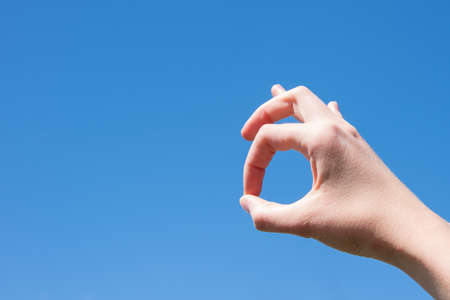 Closeup gesture of a woman hand making ok isolated against a blue sky background.の写真素材