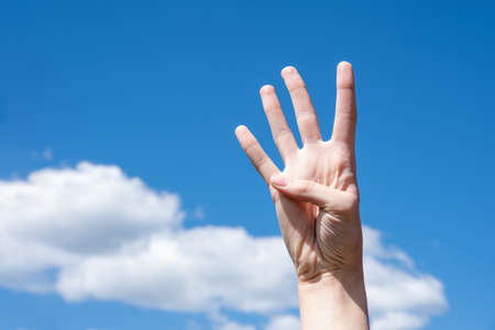 Gesture closeup of a woman's hand showing four fingers, isolated on a background of blue sky with...