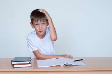 A cute boy is sitting at the table, a wound on the elbow. The child does not want to study, does not...