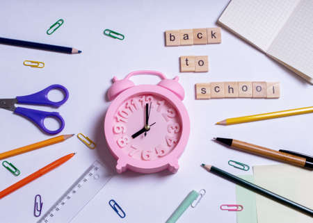 Creative flat lay top view back to school concept, summer time, education concept. Colored school supplies and pink alarm clock on white background, copy space, designの写真素材