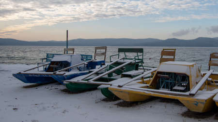 Landscape of a winter lake with multi-colored catamarans in a frozen lake and mountains. Can be used as background, postcard, design elementsの写真素材