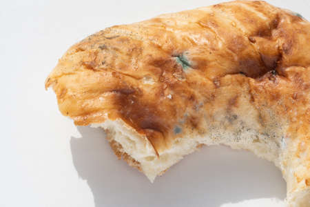 Closeup of a piece of spoiled bread with mold on a white background, copy space. The concept of...
