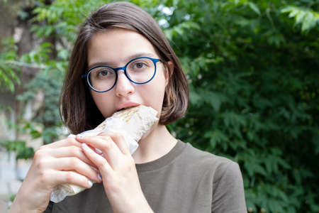 Young beautiful woman eating fast food while walking in the park, close-up. Unhealthy food concept, fast food.の写真素材