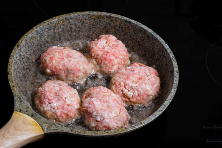 Close up of fried minced meat cutlet in frying pan over black background.